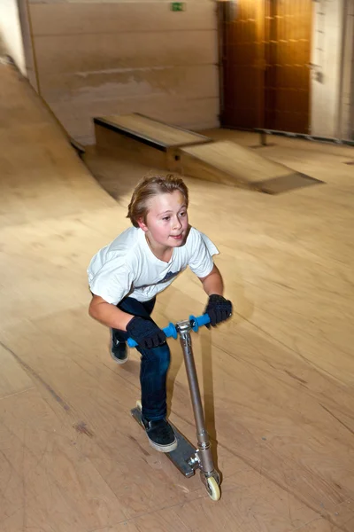 Menino está patinando com sua scooter em um salão interior — Fotografia de Stock
