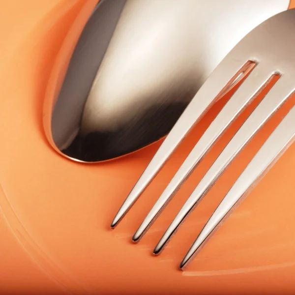 Fork and spoon on orange plate — Stock Photo, Image