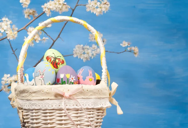 Canasta llena de coloridos huevos de Pascua sobre fondo azul — Foto de Stock