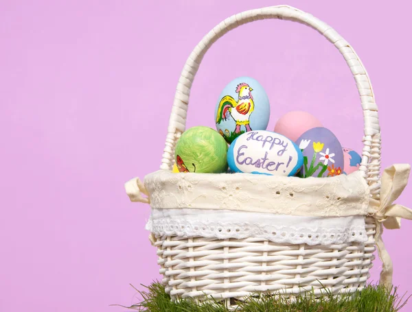 Canasta llena de coloridos huevos de Pascua sobre fondo púrpura — Foto de Stock