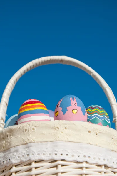 Canasta llena de coloridos huevos de Pascua pintados a mano contra el cielo azul —  Fotos de Stock