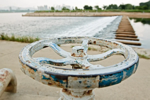 White and blue rusty industrial faucet wheel on river blurry bac — Stock Photo, Image