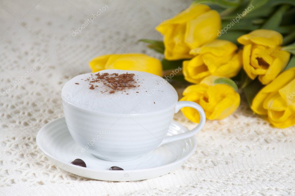 Cup of coffee on a white saucer and on the background yellow flo