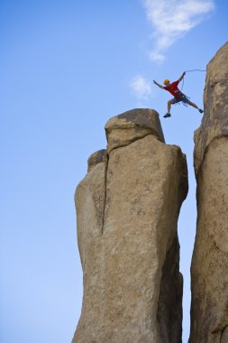 Rock climber jumping for the summit. clipart