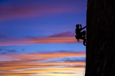 Rock climber clinging to a cliff. clipart