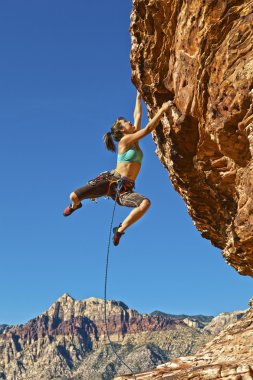 Female rock climber clinging to a cliff. clipart