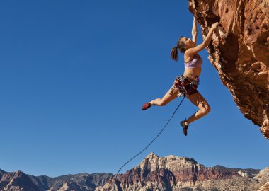 Female rock climber clinging to a cliff. clipart