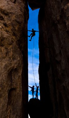 Team of climbers struggel up a steep cliff. clipart