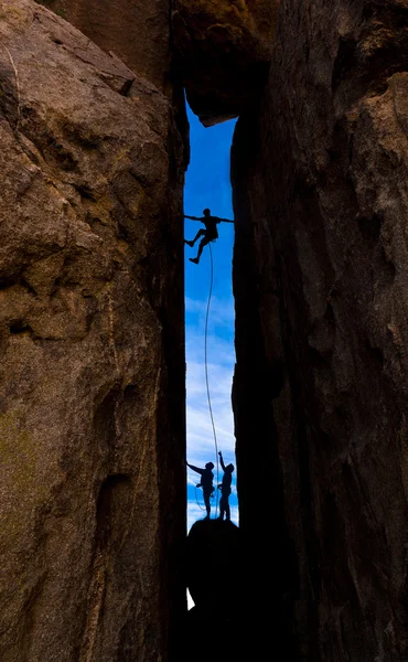 Team av klättrare kamp upp en brant klippa. — Stockfoto