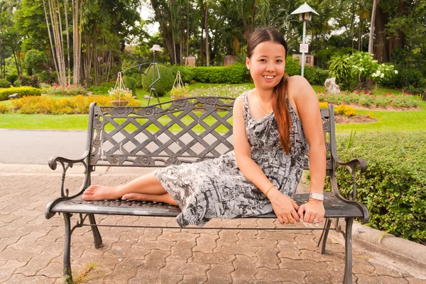 युवा आशियाई महिला बसून आणि पार्क मध्ये खंडपीठावर स्मित — स्टॉक फोटो, इमेज