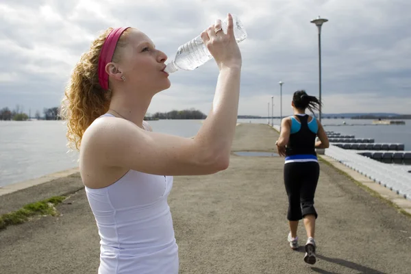Two women jogging and taking a water break