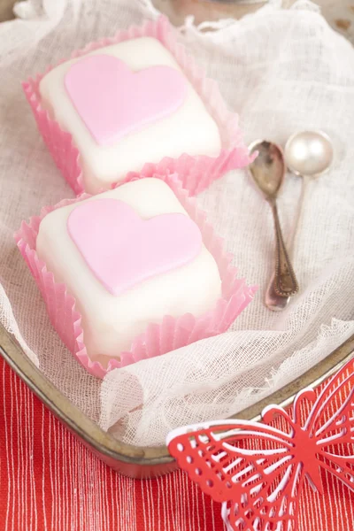 Hjärtformad rosa cupcakes i tenn bricka med skedar, röda bakgrunds — Stockfoto