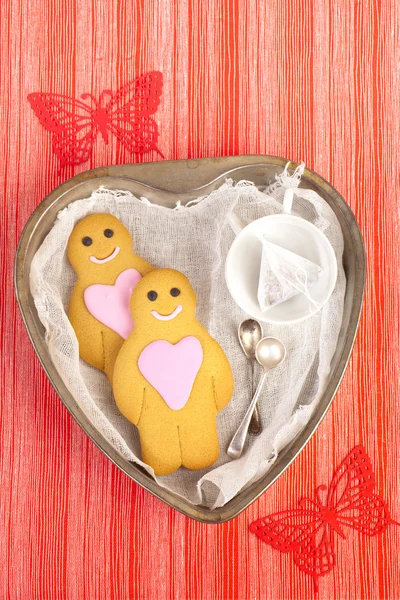 Gingerbread boy and girl on tin heart shaped tray, red linen str — Stock Photo, Image