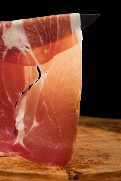 Segment van droge gerookte ham, op hout en zwarte achtergrond — Stockfoto