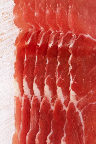 Dry cured ham slices on white wood background — Stock Photo, Image