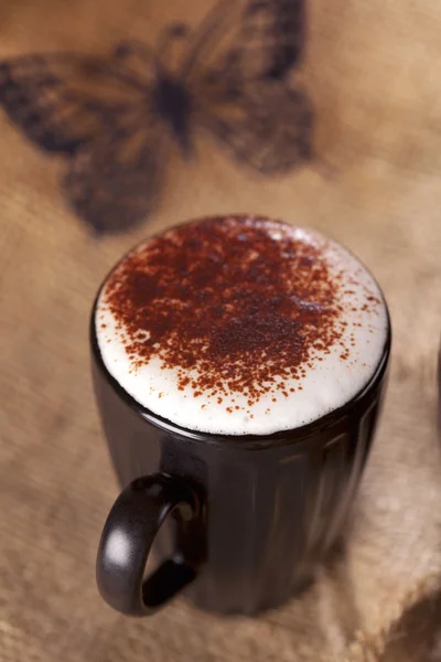 Bevanda schiumosa calda cappuccino chokolate spolverato, burro di carta nero — Foto Stock
