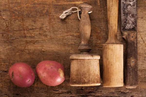 Antieke aardappel mashers en mes op oude houten tafel met rood — Stockfoto