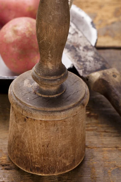 Antique potato masher on old wooden table with knife and potato — Stock Photo, Image