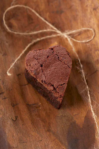 Chocolate brownie heart with bow, rough wooden background — Stock Photo, Image