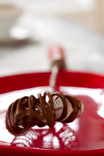 Metal whisk with melted chocolate cream on red plate — Stock Photo, Image