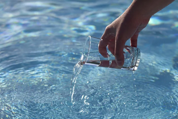 Девушки руки выливают воду, на фоне голубых вод — стоковое фото