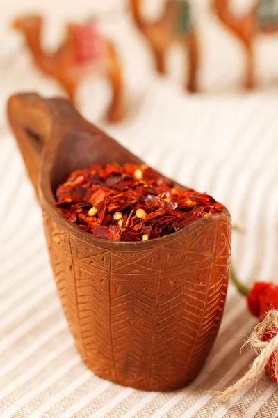 Red chillies paper flakes in curved wooden bowl and camel carava — Stock Photo, Image