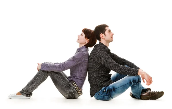 Young woman and man sitting on the floor, back to back. — Stock Photo, Image