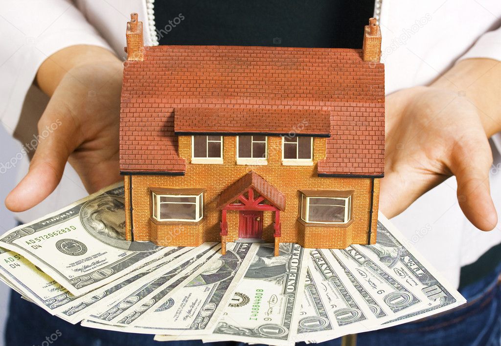 A person holding a miniature house and some dollar bills