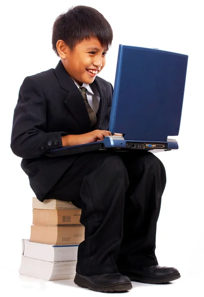 Мальчик со своим компьютером сидит на куче книг — стоковое фото