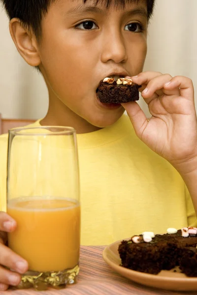 Kind isst Brownies und trinkt Orangensaft — Stockfoto