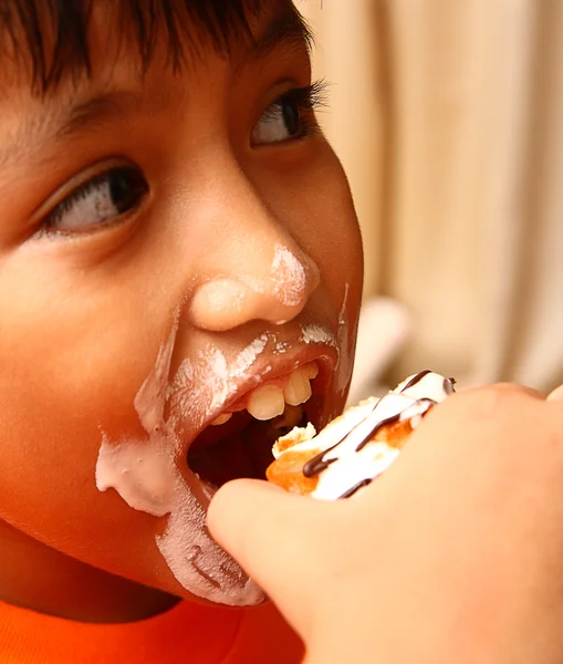 Bambino con un viso disordinato mangiare una torta alla panna — Foto Stock