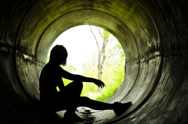 Silhouette of a young girl smoking in sewer pipe clipart