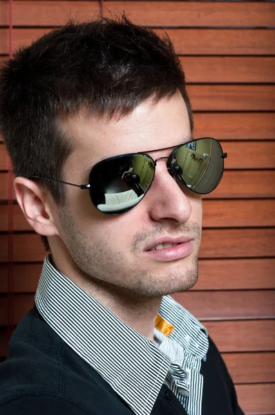 Close-up of a young man in sunglasses against blinds — Stock Photo, Image