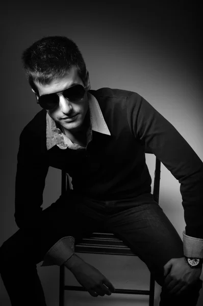 Young man sitting in chair in sunglasses in shirt in black and — Stock Photo, Image