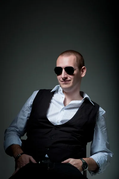 Jonge man zittend in stoel glimlachend in zonnebril — Stockfoto