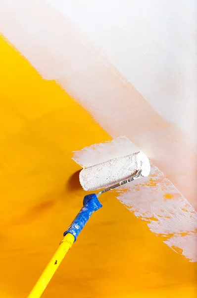 Tinta branca sobre a parede amarela com haste de pintura — Fotografia de Stock