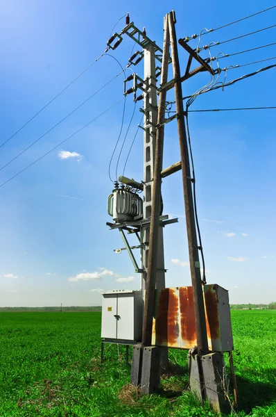 Линии электропередач против зеленого поля и голубого неба — стоковое фото