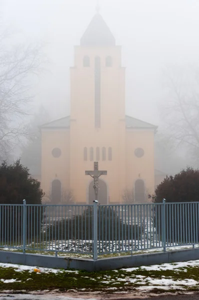 Церковь в тумане с каменным крестом и забором — стоковое фото