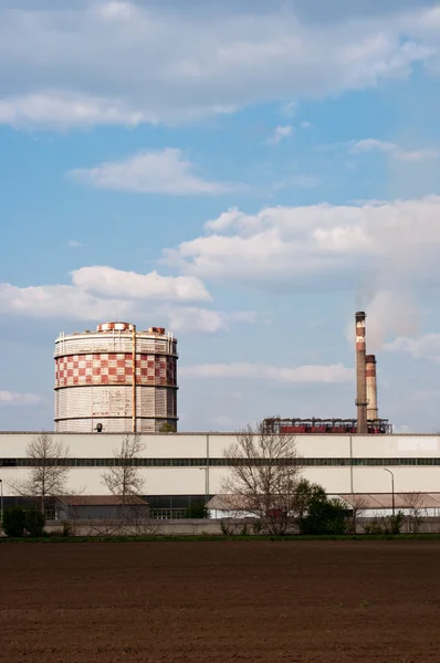 Veld met grote silo en fabriek in achtergrond tegen blauwe hemel — Stockfoto