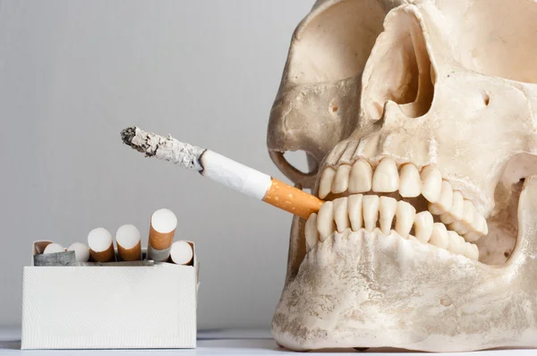 Crânio humano com cigarros contra fundo branco isolado — Fotografia de Stock