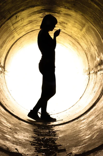 Silhouette of a young girl smoking in sewer pipe — Stock Photo, Image