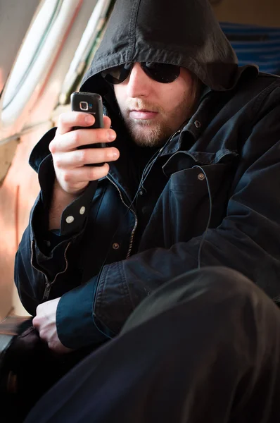 Hooded man looking at his cellular phone in an old airplane — Stock Photo, Image