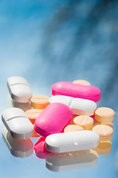 Pílulas brancas roxas e amarelas com reflexão sobre o fundo azul — Fotografia de Stock