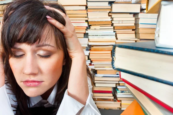 Faculdade menina segurando a cabeça contra muitos livros — Fotografia de Stock