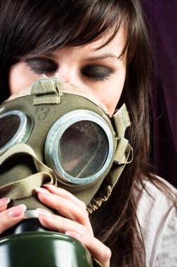 Beautiful girl is holding an old gasmask against dark background clipart