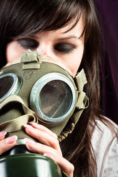 Beautiful girl is holding an old gasmask against dark background — Stock Photo, Image