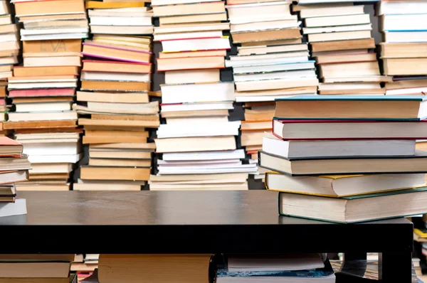Books piled up against black desk — Stock Photo, Image