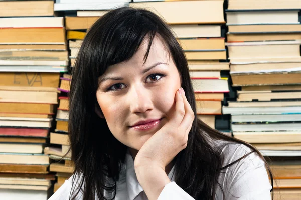 Junge Studentin denkt gegen aufgetürmte Bücher — Stockfoto