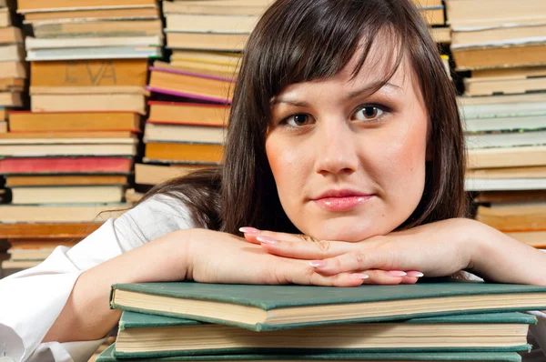Portrait of a young student against piled up books — Stock Photo, Image