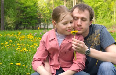 The father and the daughter on a green meadow with dandelions clipart